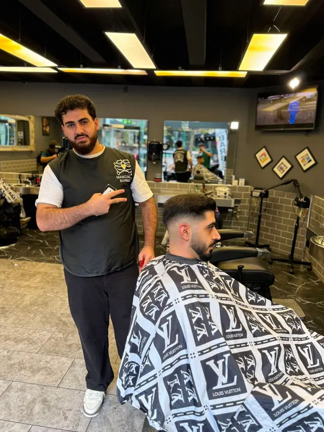 A barber standing beside his client in the chair, giving a peace sign