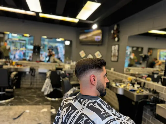A client with a fresh fade and beard in the chair, the shop floor behind him
